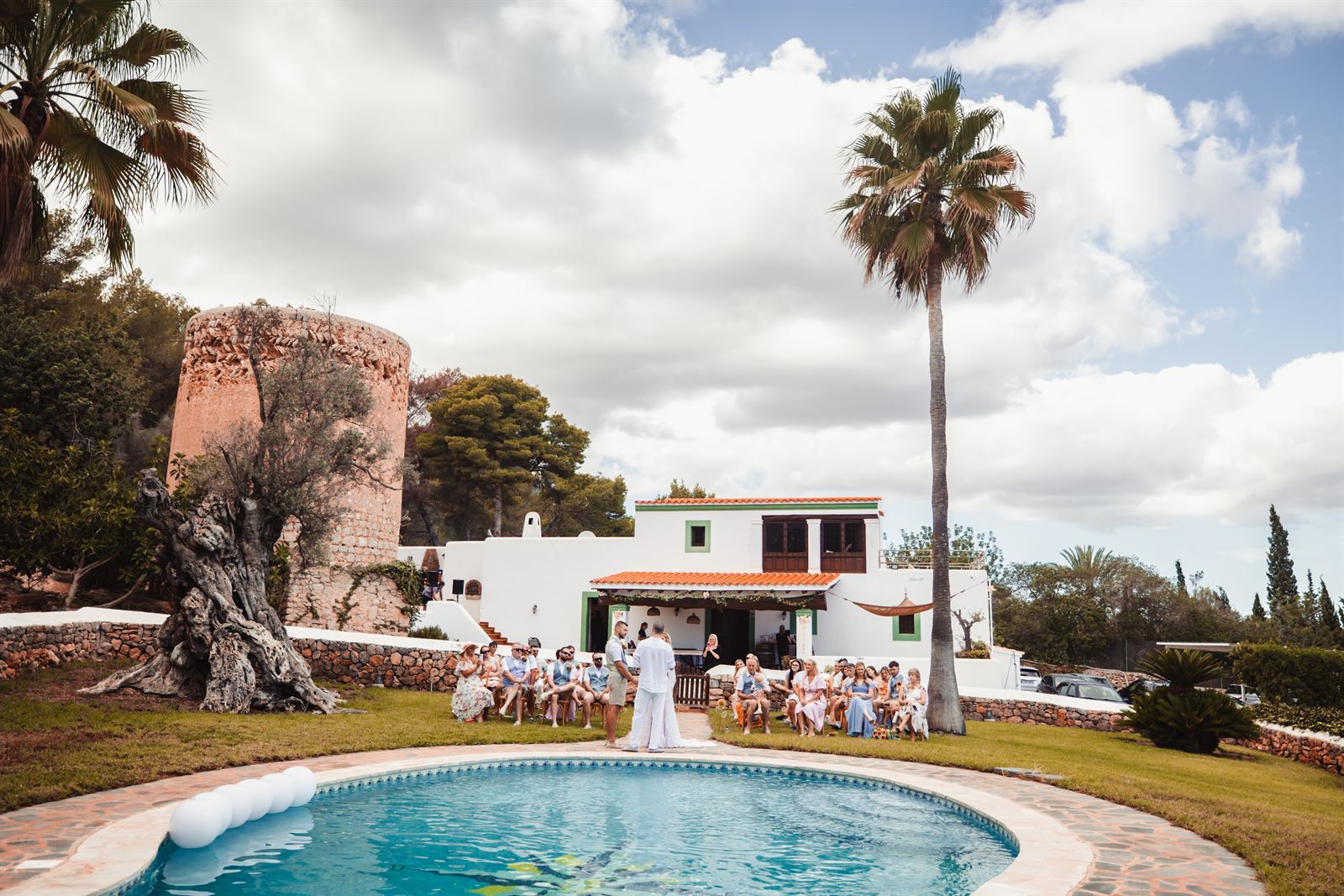 A wedding ceremony on the lawn by the pool, in front of the farmhouse and tower