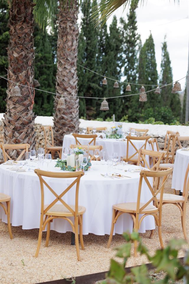 Round dinner tables with white cloths beneath tall palm trees