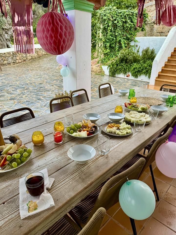 Long wooden table laid for a birthday lunch on the terrace, with balloons